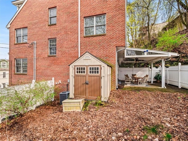 rear view of property with an outbuilding, a storage shed, a patio, fence, and brick siding