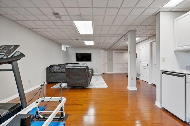 exercise area featuring a paneled ceiling, light wood-type flooring, baseboards, and visible vents