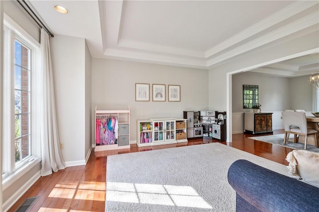 living area featuring visible vents, baseboards, crown molding, a tray ceiling, and wood finished floors