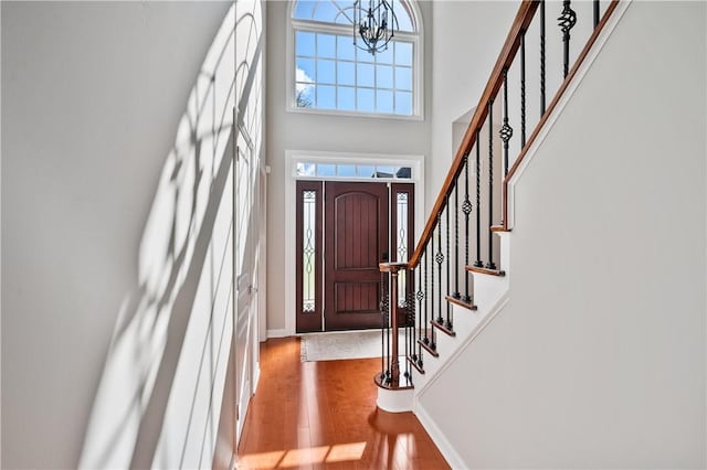 foyer featuring stairway, wood finished floors, a high ceiling, a notable chandelier, and baseboards