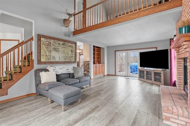 living room with baseboards, stairway, a brick fireplace, visible vents, and wood finished floors