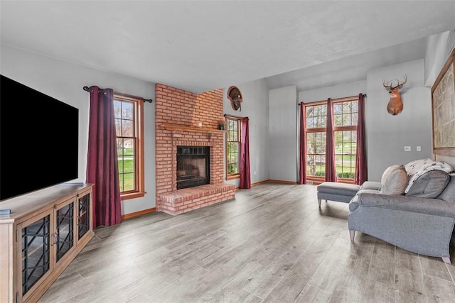 living room featuring wood finished floors, baseboards, and a brick fireplace