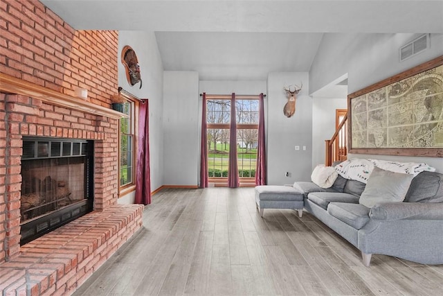 living room with wood finished floors, a brick fireplace, vaulted ceiling, and visible vents