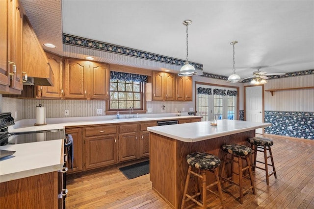 kitchen featuring a kitchen breakfast bar, light countertops, a kitchen island, black electric range oven, and a sink
