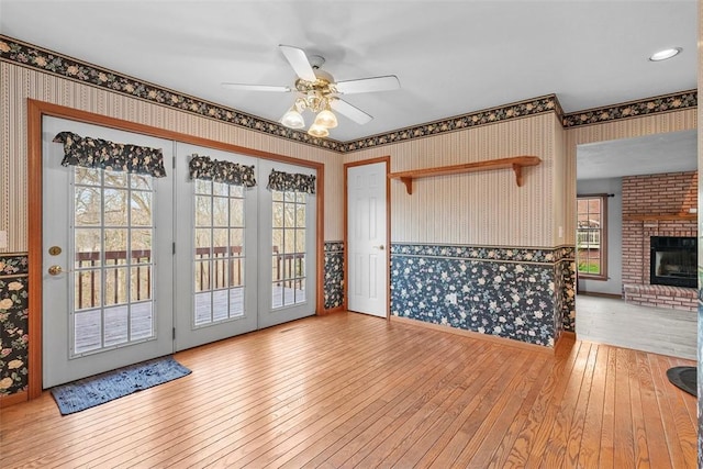 unfurnished living room featuring a fireplace, hardwood / wood-style flooring, wallpapered walls, and a ceiling fan