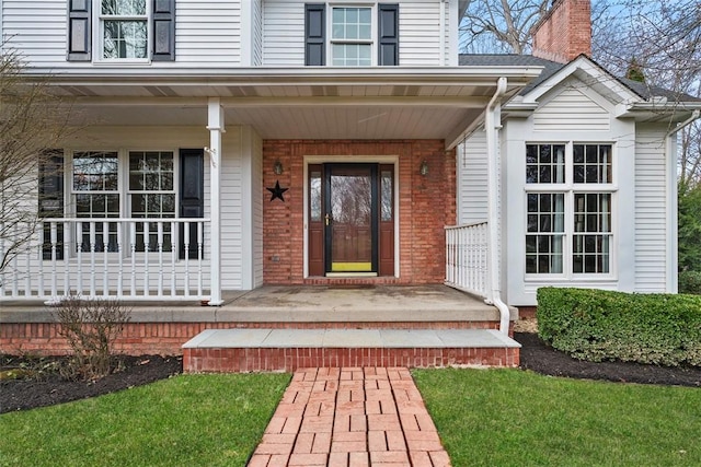property entrance featuring brick siding, covered porch, and a chimney