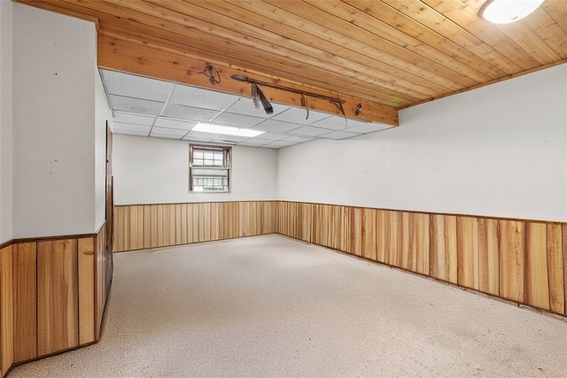 basement featuring wooden walls, a drop ceiling, wainscoting, and wood ceiling