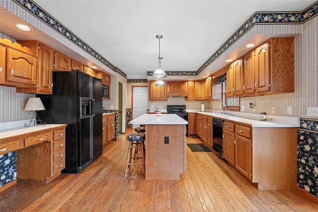kitchen with a sink, black appliances, a kitchen breakfast bar, and wallpapered walls