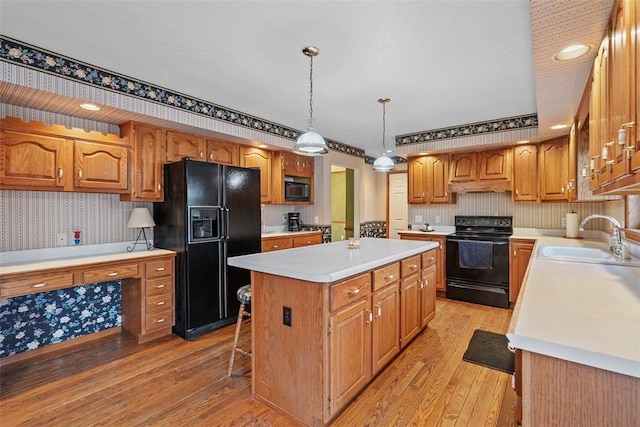 kitchen featuring a center island, a sink, light countertops, black appliances, and wallpapered walls