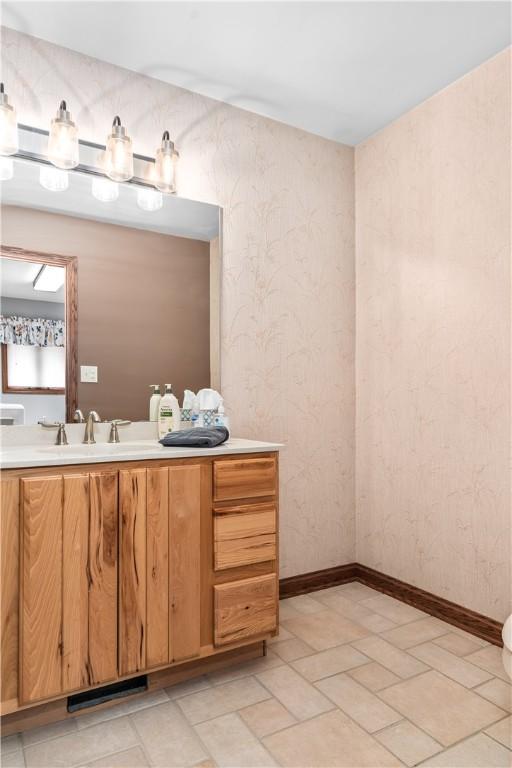 bathroom featuring vanity, baseboards, and wallpapered walls