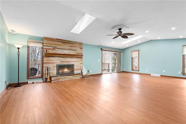 unfurnished living room with vaulted ceiling with skylight, a ceiling fan, a stone fireplace, wood finished floors, and baseboards