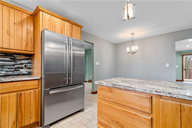 kitchen featuring light stone countertops, an inviting chandelier, high end refrigerator, decorative light fixtures, and backsplash
