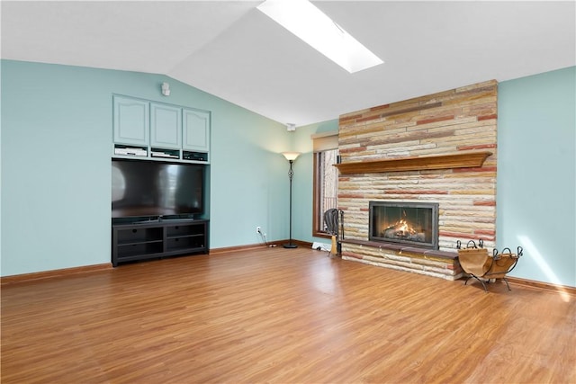 unfurnished living room featuring a stone fireplace, light wood finished floors, lofted ceiling with skylight, and baseboards