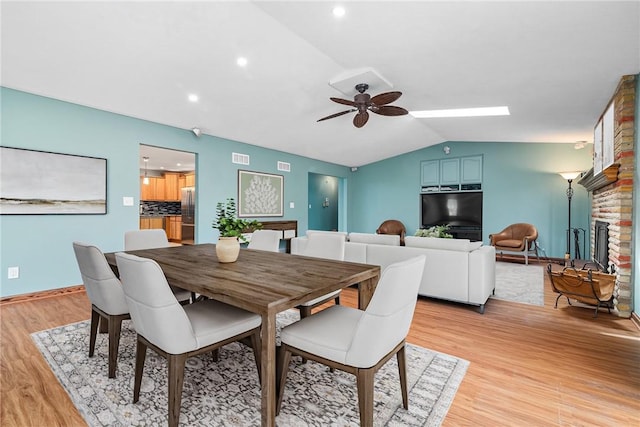 dining space featuring a brick fireplace, light wood-style flooring, a ceiling fan, recessed lighting, and lofted ceiling
