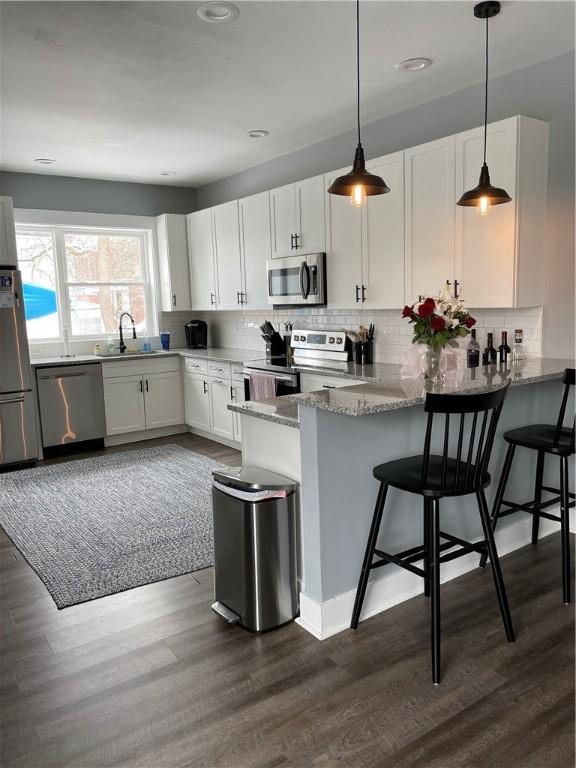 kitchen featuring light stone countertops, tasteful backsplash, a peninsula, a sink, and stainless steel appliances