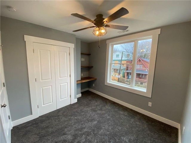 unfurnished bedroom with a closet, dark colored carpet, visible vents, and baseboards