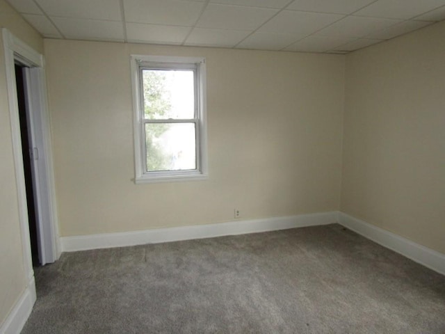 carpeted empty room featuring a paneled ceiling and baseboards