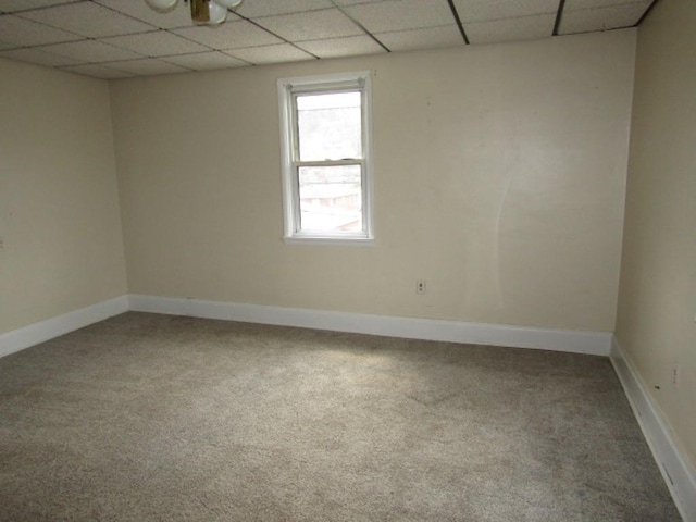 carpeted empty room featuring baseboards and a drop ceiling