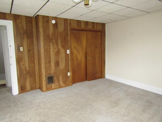unfurnished bedroom with visible vents, a closet, carpet floors, wood walls, and a drop ceiling