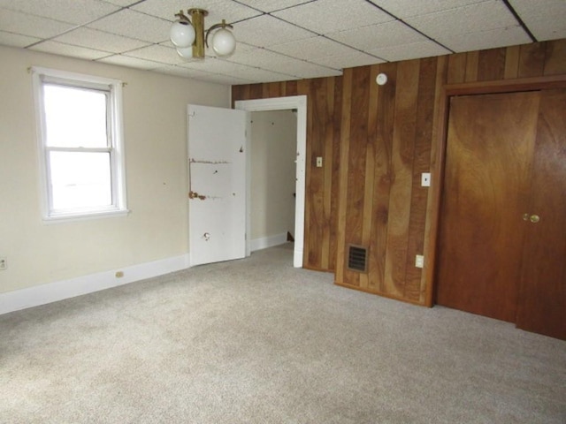 carpeted spare room with wood walls, baseboards, and a drop ceiling
