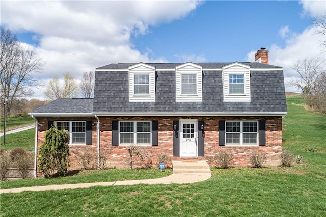 view of front of property with a front yard, brick siding, a chimney, and a shingled roof