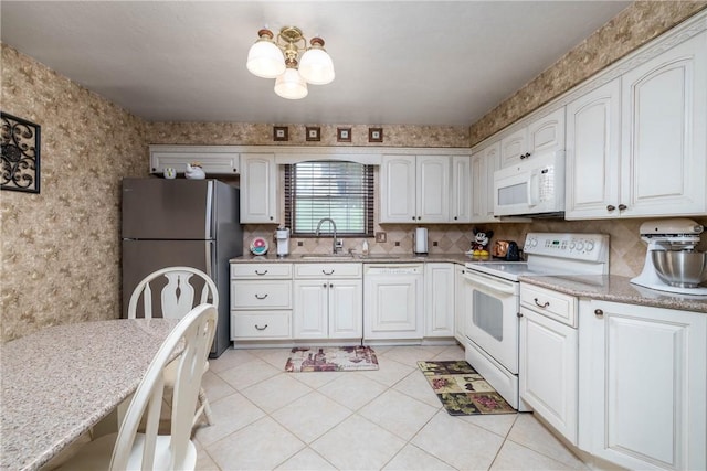 kitchen featuring white appliances, light stone countertops, white cabinetry, a sink, and wallpapered walls