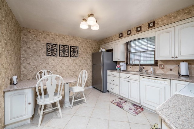 kitchen featuring freestanding refrigerator, paneled dishwasher, white cabinets, a sink, and wallpapered walls