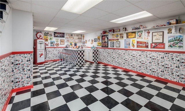 interior space with tile patterned floors, a wainscoted wall, and a drop ceiling
