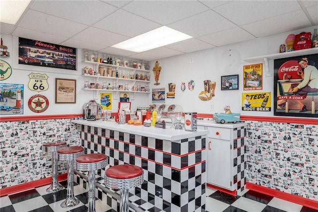 bar featuring tile patterned floors, a drop ceiling, and a wainscoted wall