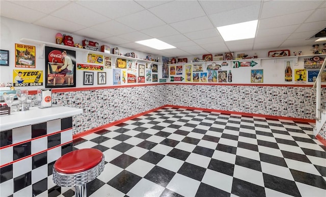 misc room with tile patterned floors, a paneled ceiling, and wainscoting
