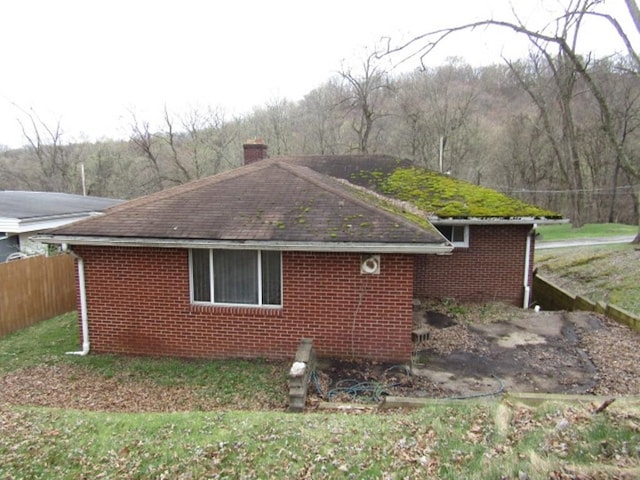 view of side of property with fence, brick siding, and a chimney