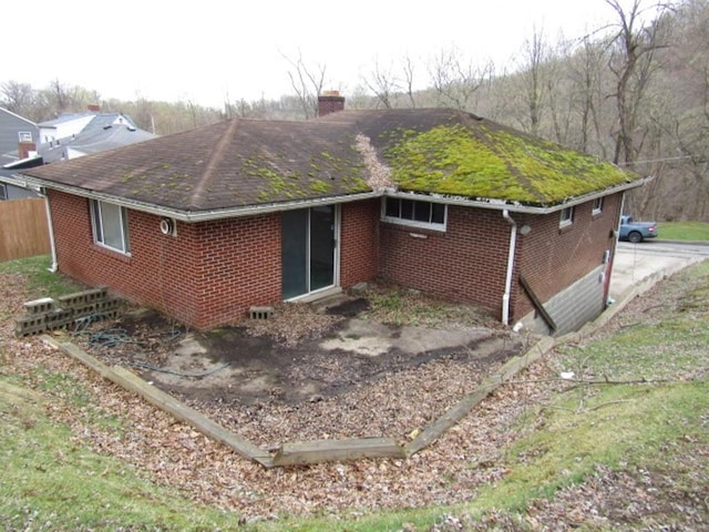 view of property exterior with brick siding, roof with shingles, fence, and a chimney