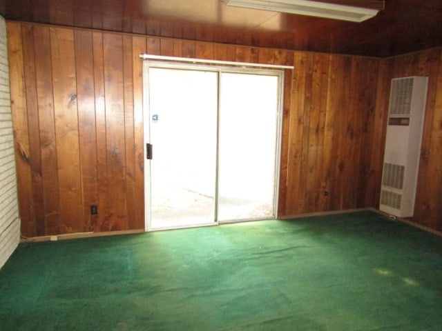 carpeted empty room with wooden walls and a heating unit