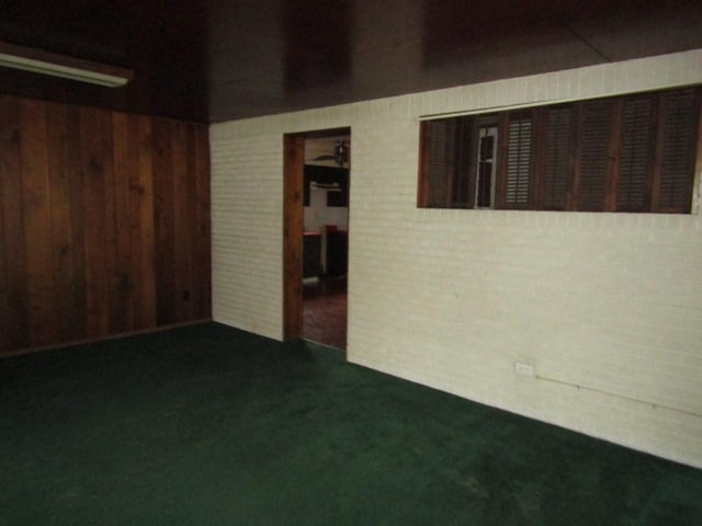 spare room featuring dark carpet, brick wall, and wooden walls