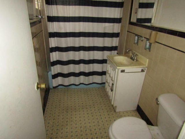 bathroom with toilet, vanity, shower / bath combination with curtain, and tile walls