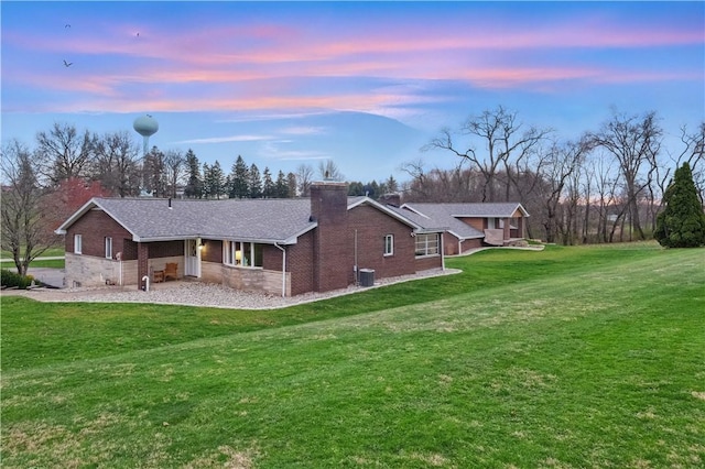 exterior space featuring cooling unit, a chimney, brick siding, and a lawn