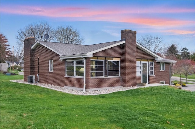 property exterior at dusk featuring central AC, a chimney, brick siding, and a yard