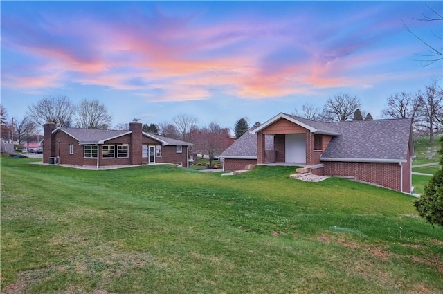 back of property at dusk with a yard and brick siding