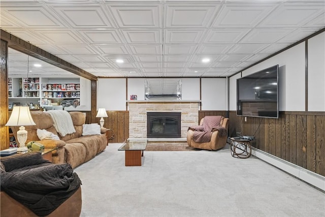 living room with a baseboard heating unit, wooden walls, wainscoting, and a stone fireplace