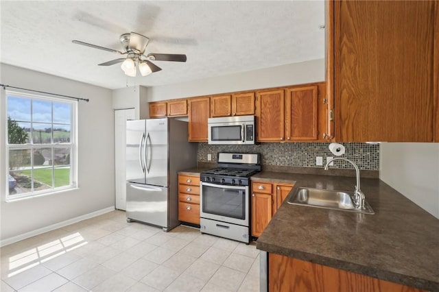 kitchen with dark countertops, brown cabinetry, decorative backsplash, stainless steel appliances, and a sink