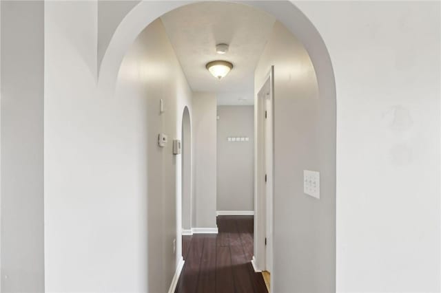 hallway featuring arched walkways, dark wood-style flooring, and baseboards