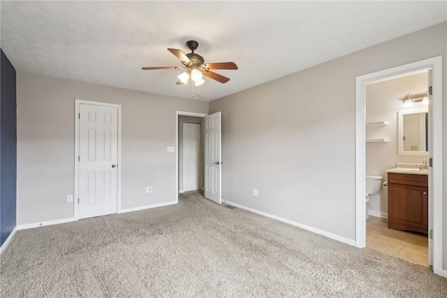 unfurnished bedroom featuring ceiling fan, ensuite bathroom, light carpet, a sink, and baseboards