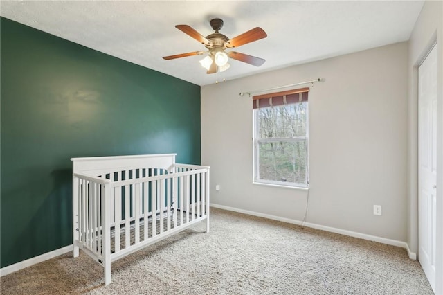 unfurnished bedroom with carpet, baseboards, a ceiling fan, and a nursery area