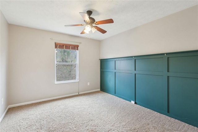 carpeted spare room featuring baseboards and a ceiling fan