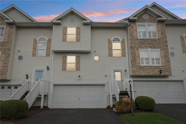 townhome / multi-family property with aphalt driveway, stone siding, and an attached garage