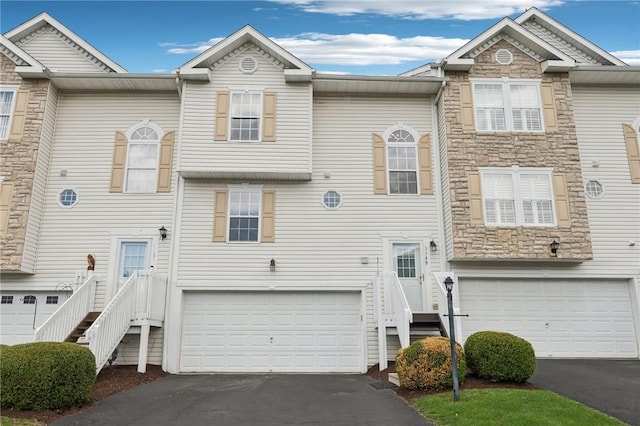 view of property featuring a garage, aphalt driveway, and stone siding