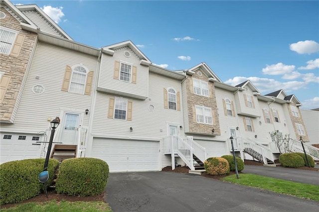 multi unit property with a residential view, a garage, stone siding, and aphalt driveway