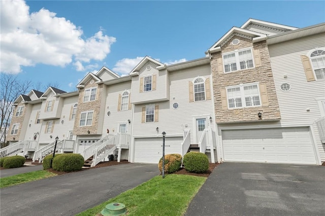 townhome / multi-family property with an attached garage, a residential view, driveway, and stone siding