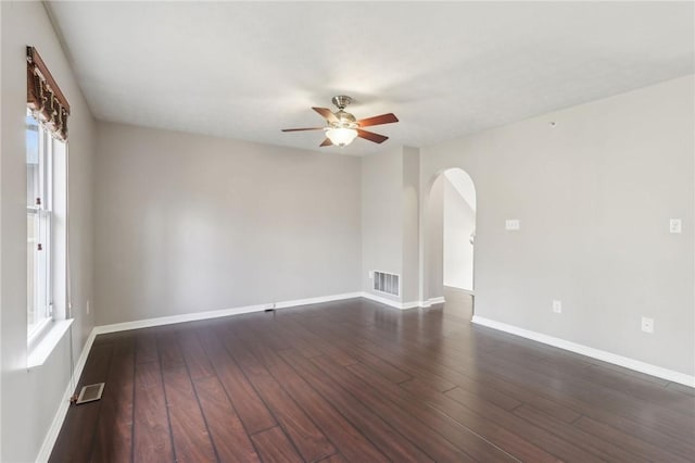empty room with arched walkways, wood-type flooring, a ceiling fan, and visible vents