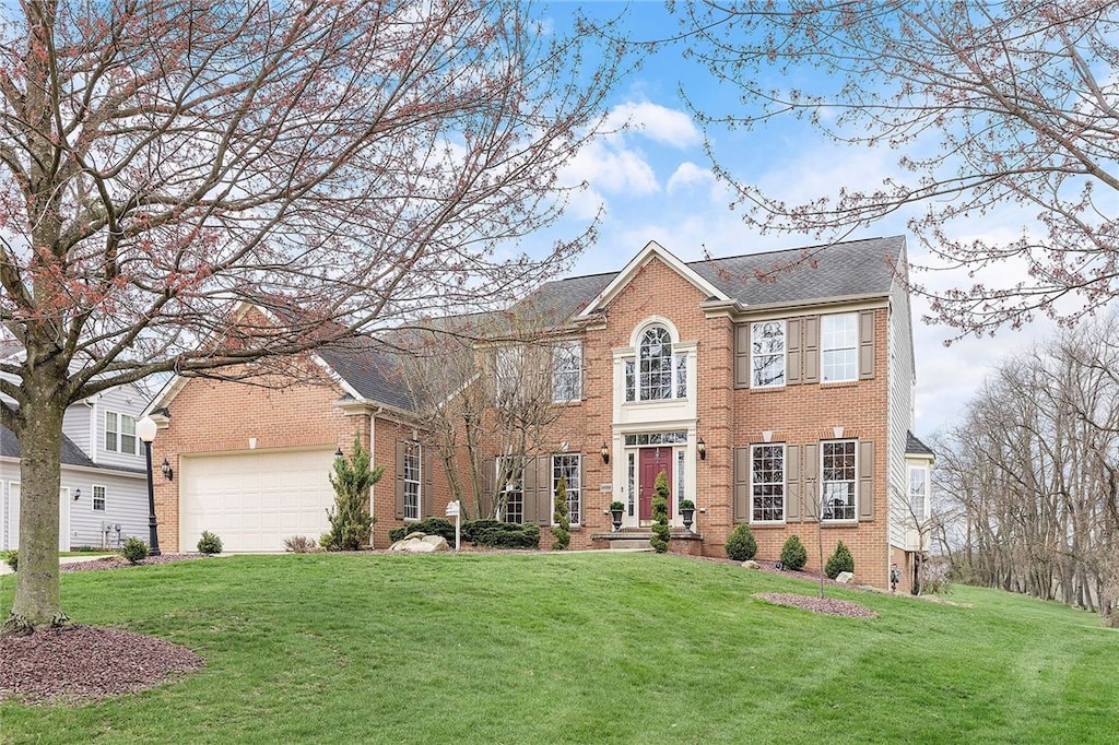colonial-style house with an attached garage, roof with shingles, a front lawn, and brick siding